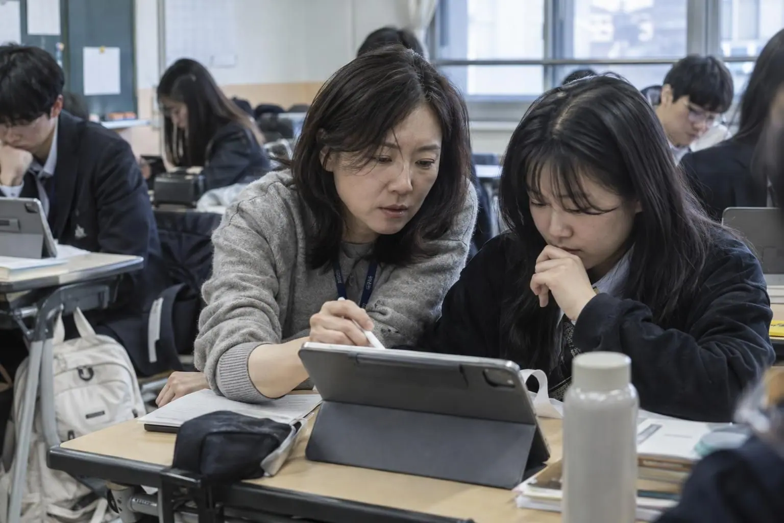 선생님이 학생 옆에서 태블릿으로 과제를 함께 보는 모습