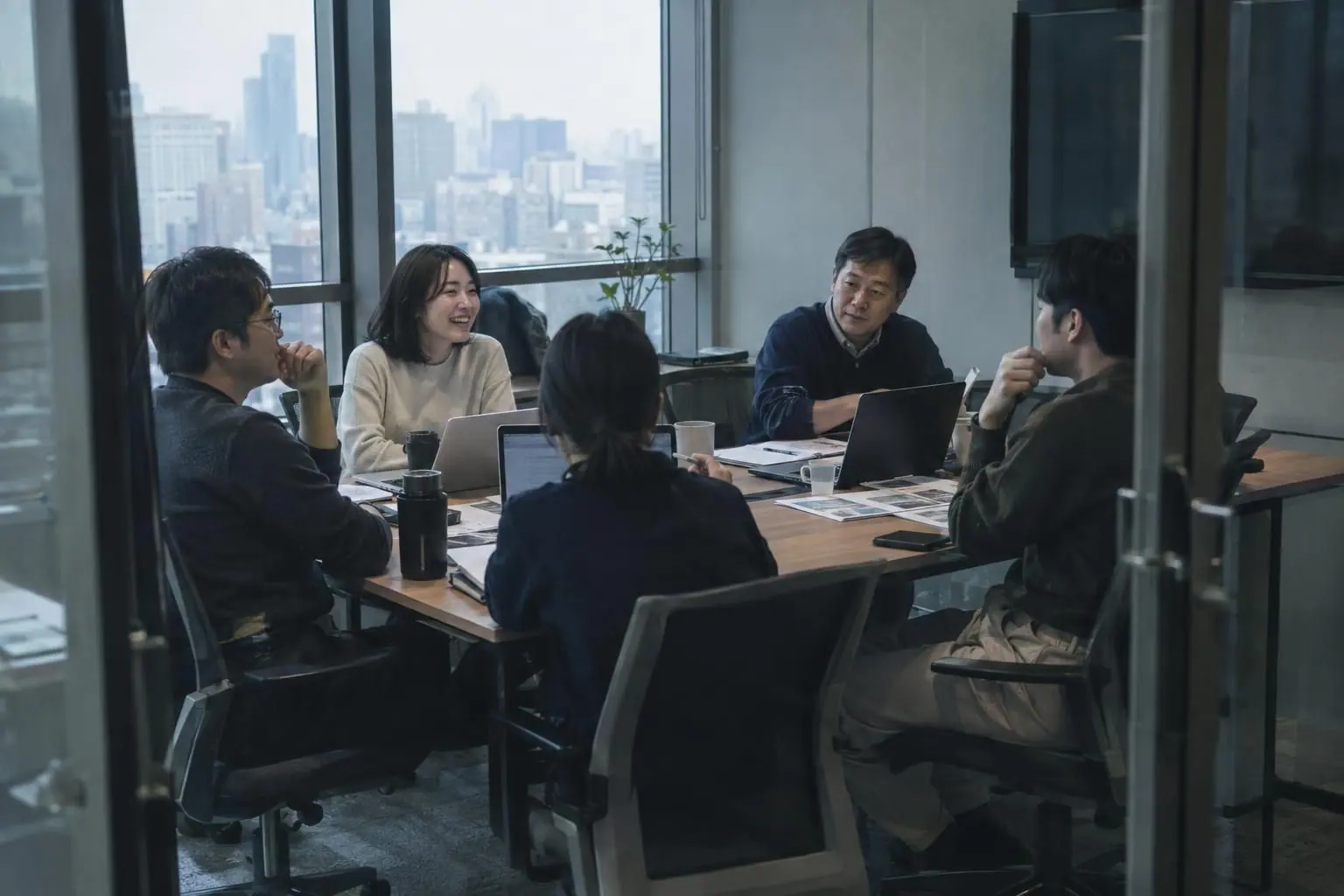 회의실에서 다섯 명의 팀원이 노트북을 펴 놓고 웃으며 이야기하는 모습